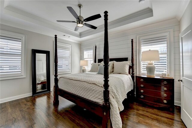 bedroom with ornamental molding, a tray ceiling, baseboards, and wood finished floors