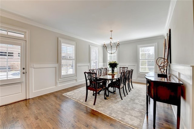 dining space featuring an inviting chandelier, crown molding, wood finished floors, and a wainscoted wall