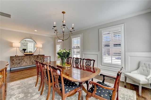 dining space with wood finished floors, visible vents, crown molding, and an inviting chandelier