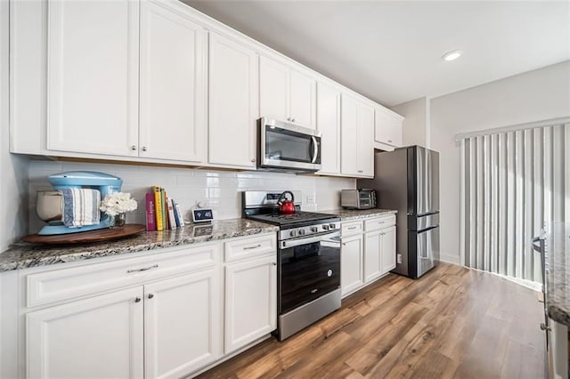 kitchen with light stone countertops, wood finished floors, stainless steel appliances, white cabinets, and backsplash