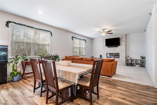 dining room featuring ceiling fan, a premium fireplace, and light wood-style flooring