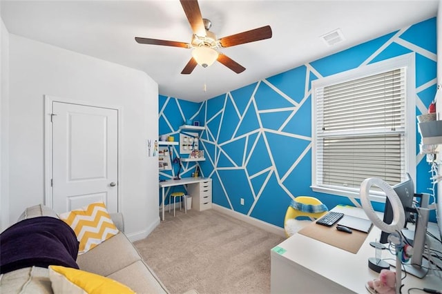 carpeted home office featuring an accent wall, a ceiling fan, visible vents, and baseboards