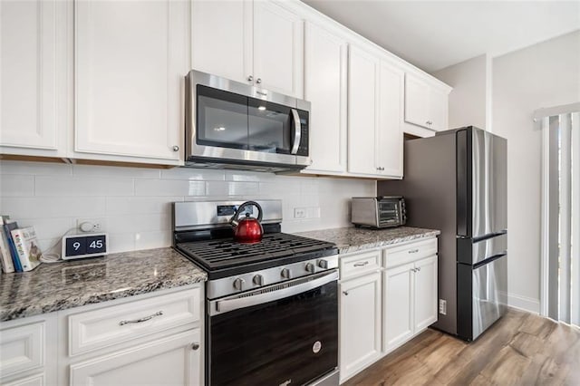 kitchen featuring light stone counters, stainless steel appliances, backsplash, and white cabinetry