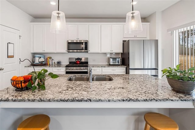 kitchen featuring a breakfast bar, appliances with stainless steel finishes, hanging light fixtures, white cabinetry, and a sink