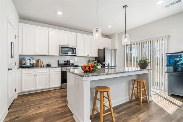 kitchen featuring visible vents, a kitchen bar, stainless steel appliances, white cabinetry, and dark wood-style flooring