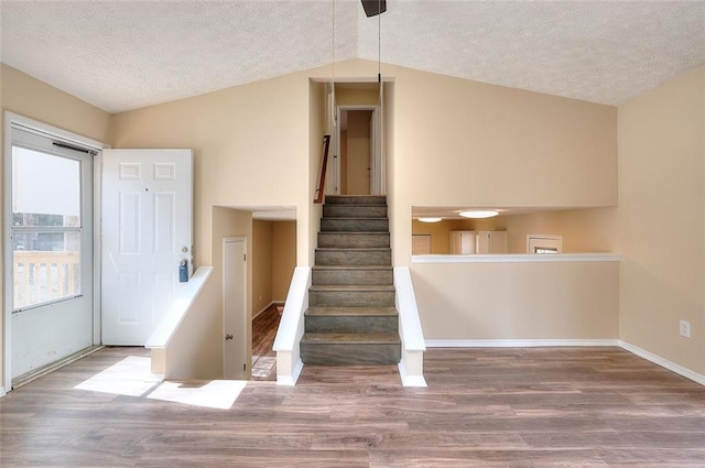 stairs with lofted ceiling, a textured ceiling, baseboards, and wood finished floors