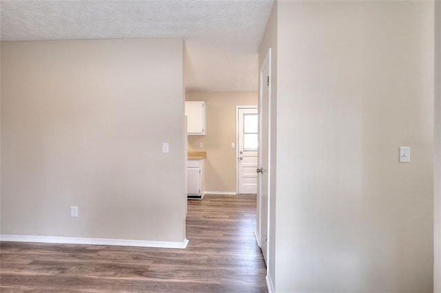 hallway with dark wood-style floors, a textured ceiling, and baseboards