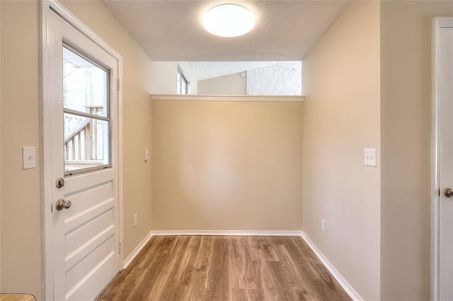 doorway featuring a textured ceiling, baseboards, vaulted ceiling, and wood finished floors