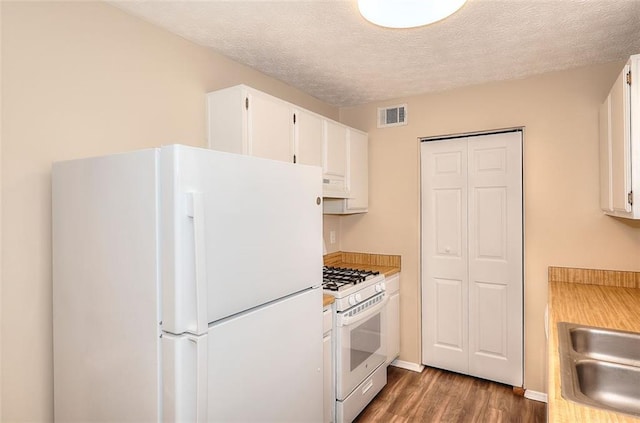 kitchen with visible vents, white cabinets, a textured ceiling, wood finished floors, and white appliances