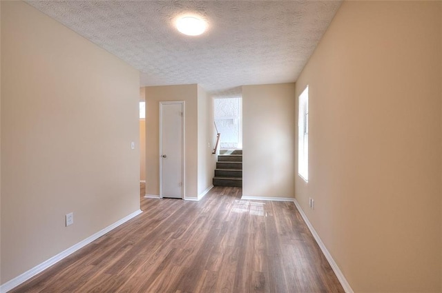 empty room with a textured ceiling, stairway, wood finished floors, and baseboards