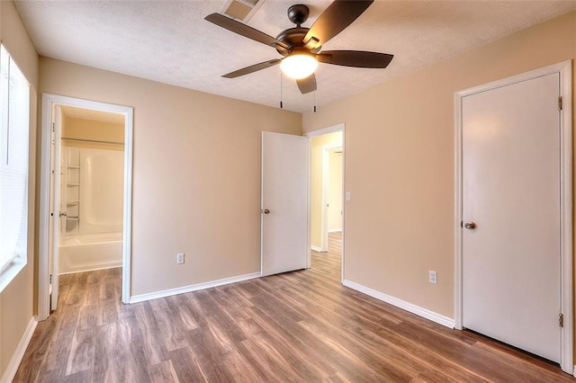 unfurnished bedroom with ceiling fan, a textured ceiling, ensuite bath, wood finished floors, and baseboards