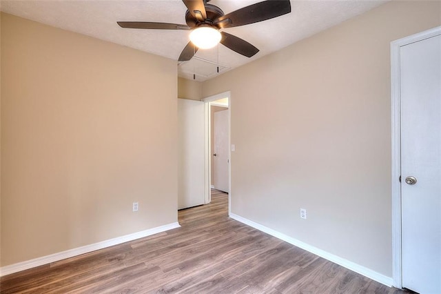 empty room featuring ceiling fan, attic access, baseboards, and wood finished floors