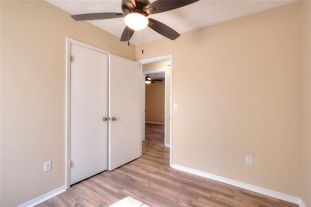 unfurnished bedroom featuring baseboards, ceiling fan, a textured ceiling, and light wood-style floors