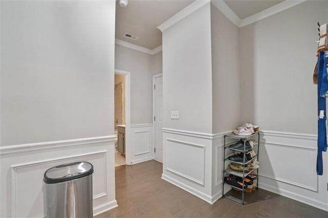 corridor with visible vents, crown molding, wood finished floors, and a decorative wall