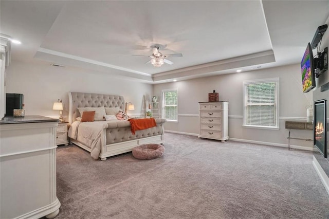 bedroom with carpet floors, visible vents, a glass covered fireplace, baseboards, and a raised ceiling