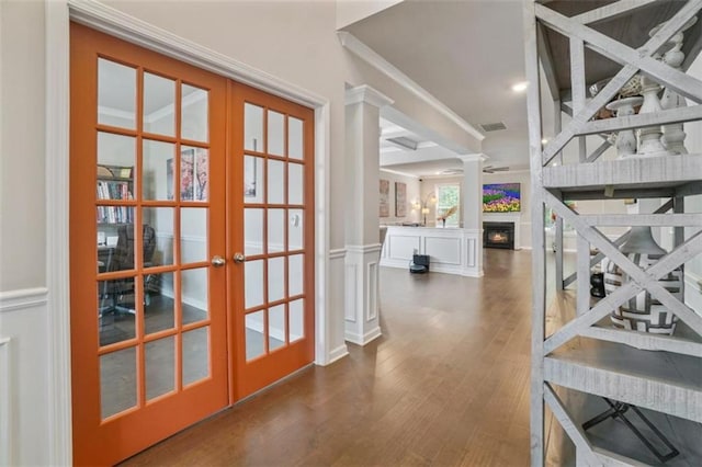interior space with decorative columns, french doors, wood finished floors, ornamental molding, and a decorative wall