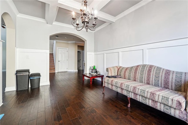 living room featuring dark wood-style flooring, ornamental molding, a chandelier, coffered ceiling, and beamed ceiling