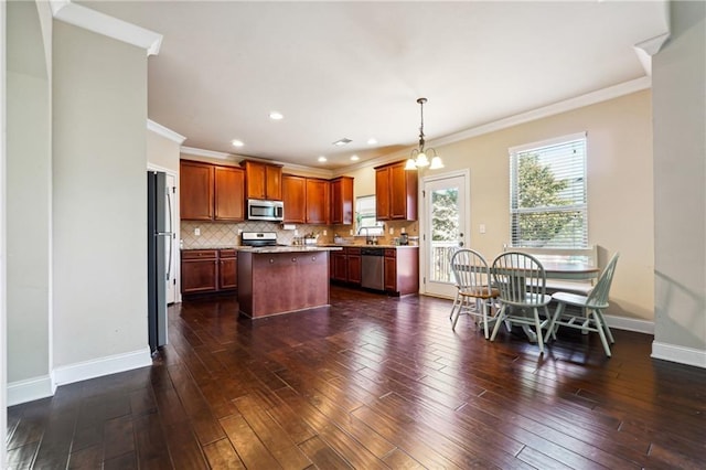 kitchen featuring stainless steel appliances, baseboards, backsplash, a center island, and dark wood finished floors