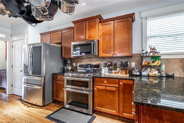 kitchen with backsplash, ornamental molding, stainless steel appliances, dark stone countertops, and light hardwood / wood-style floors