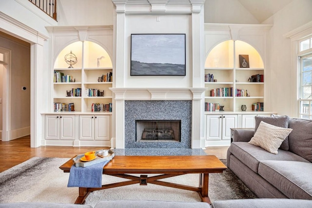 living room featuring lofted ceiling, hardwood / wood-style floors, built in shelves, and a high end fireplace