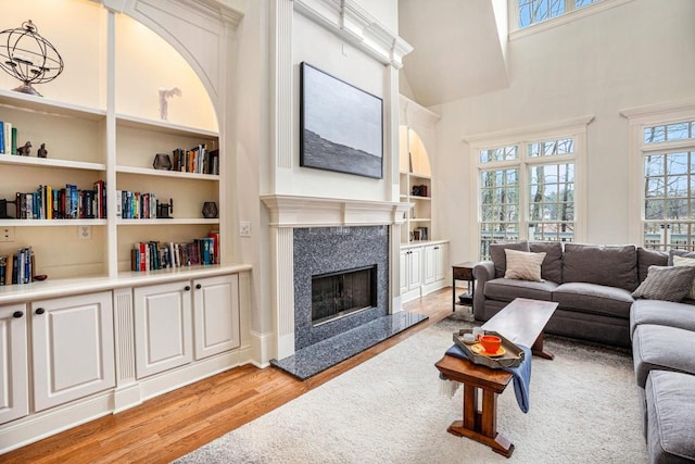 living room featuring a towering ceiling, light hardwood / wood-style flooring, a premium fireplace, and built in shelves