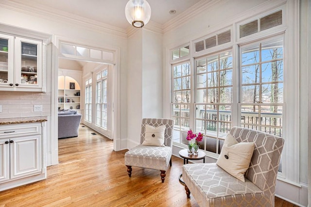 sitting room featuring ornamental molding, light wood-type flooring, and built in shelves