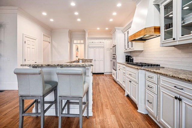 kitchen with a center island with sink, custom range hood, white cabinets, and appliances with stainless steel finishes