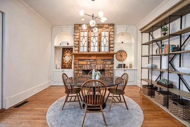 dining space featuring ornamental molding, light hardwood / wood-style floors, built in shelves, a stone fireplace, and a chandelier