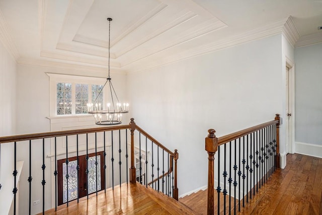 stairs with a raised ceiling, ornamental molding, hardwood / wood-style floors, and a notable chandelier