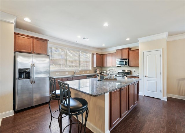 kitchen featuring a center island, crown molding, dark wood-type flooring, stainless steel appliances, and dark stone counters