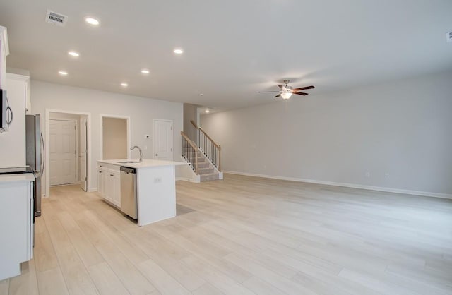 kitchen with ceiling fan, appliances with stainless steel finishes, white cabinetry, light hardwood / wood-style floors, and a center island with sink