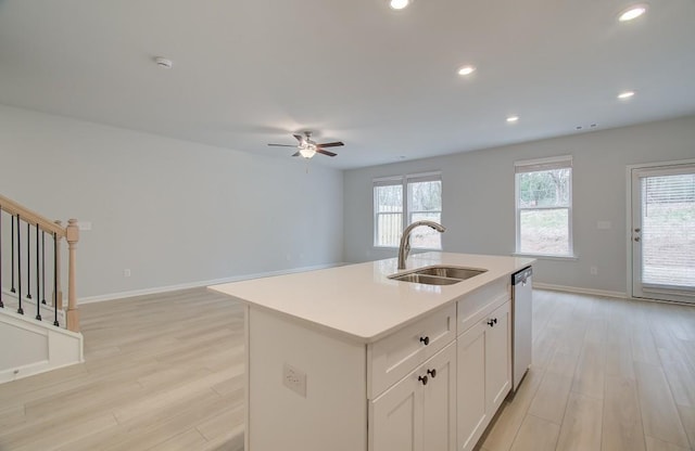 kitchen with an island with sink, dishwasher, sink, white cabinets, and light hardwood / wood-style floors