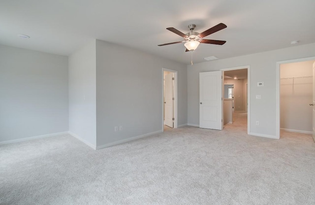 unfurnished bedroom featuring ceiling fan, a walk in closet, a closet, and light carpet