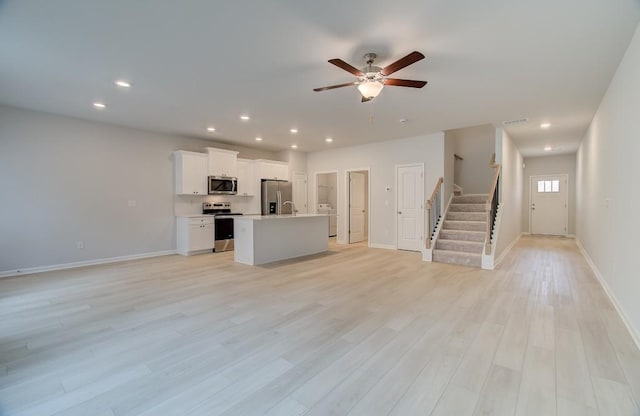 unfurnished living room with ceiling fan, washer / dryer, and light hardwood / wood-style flooring