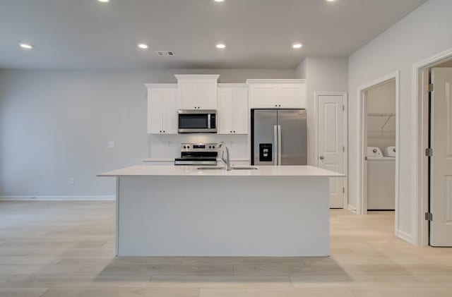 kitchen featuring appliances with stainless steel finishes, an island with sink, sink, white cabinets, and independent washer and dryer