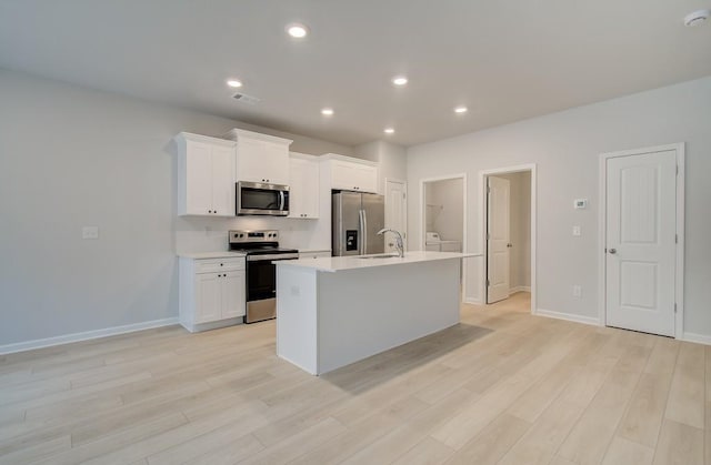 kitchen with sink, white cabinetry, stainless steel appliances, light hardwood / wood-style floors, and an island with sink