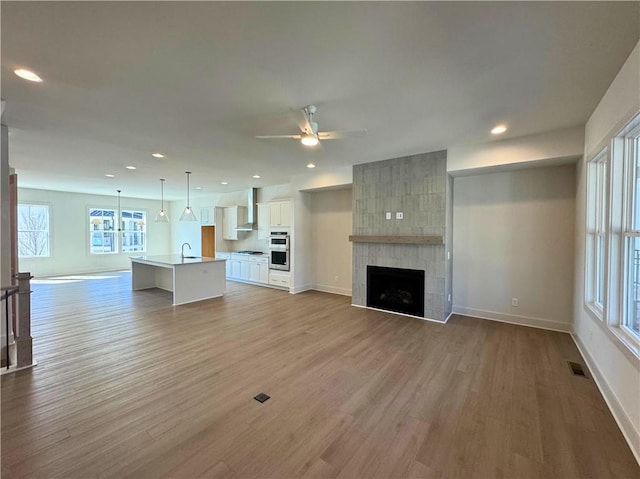 unfurnished living room featuring a fireplace, light wood finished floors, visible vents, ceiling fan, and baseboards