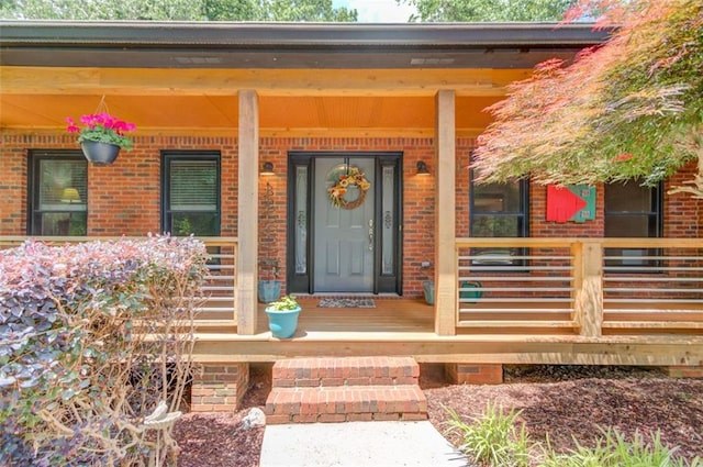 view of exterior entry featuring brick siding and covered porch