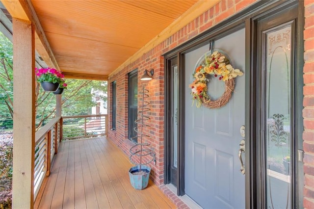 doorway to property featuring covered porch and brick siding