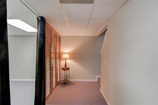 hall with a drop ceiling, carpet, and baseboards