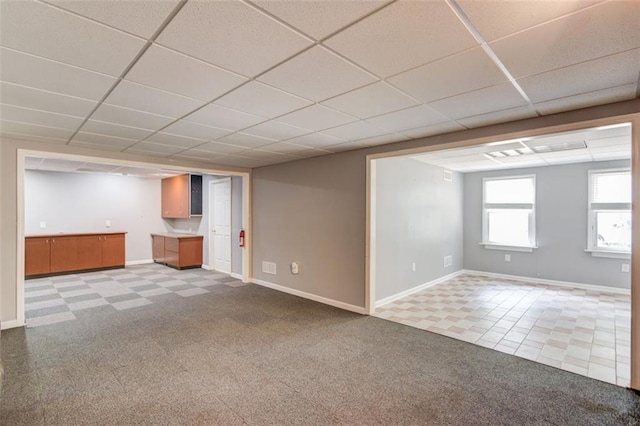 unfurnished living room featuring light carpet, a drop ceiling, and baseboards