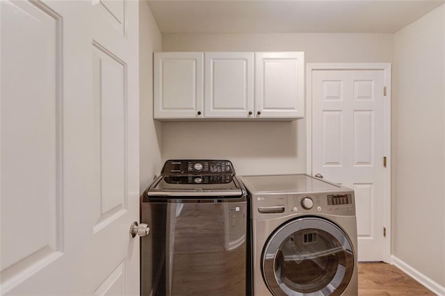 laundry room featuring cabinet space, washing machine and clothes dryer, light wood-style flooring, and baseboards