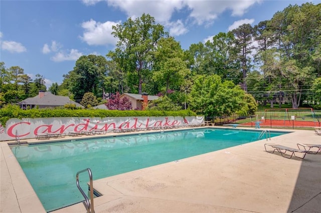 community pool with fence, a patio area, and view of scattered trees