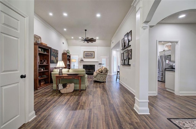 living area featuring a ceiling fan, arched walkways, a fireplace, baseboards, and dark wood-style floors