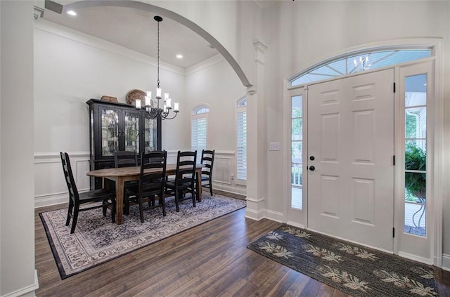 foyer featuring ornamental molding, a high ceiling, arched walkways, dark wood finished floors, and a notable chandelier