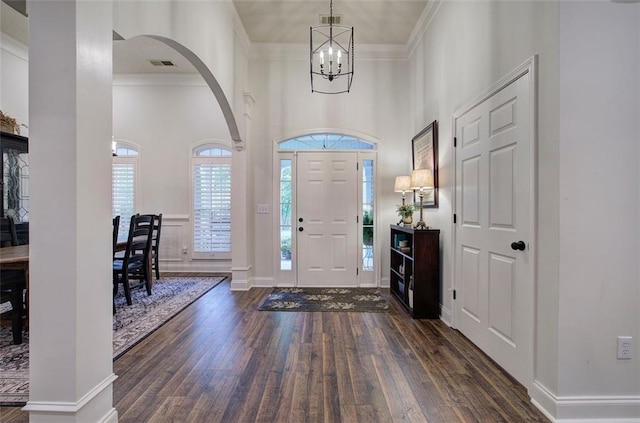 foyer entrance featuring crown molding, arched walkways, a chandelier, wood finished floors, and visible vents