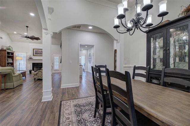 dining space featuring dark wood-style flooring, arched walkways, a fireplace, ceiling fan with notable chandelier, and recessed lighting