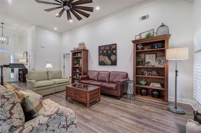 living area with a towering ceiling, crown molding, visible vents, wood finished floors, and ceiling fan with notable chandelier