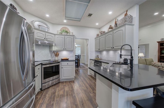 kitchen with a breakfast bar area, a sink, a peninsula, under cabinet range hood, and stainless steel appliances
