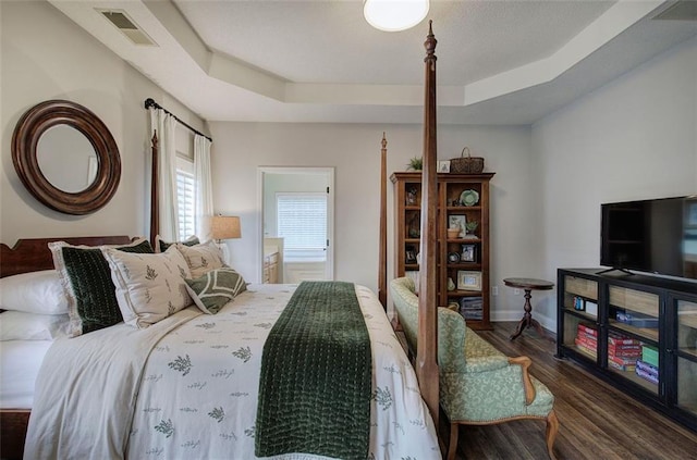 bedroom featuring a raised ceiling, baseboards, wood finished floors, and visible vents